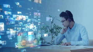 young man in glasses stares at computer screen on right as composite of many onscreen events occupies left half.